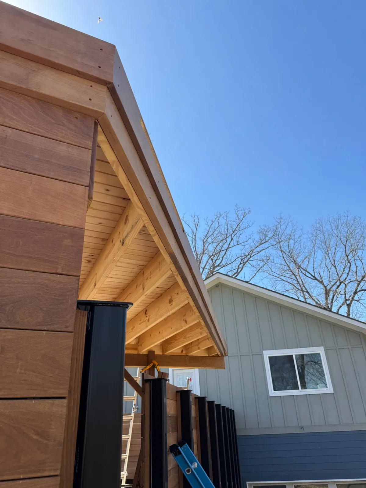 Cedar eave with black posts meeting an ipe privacy wall